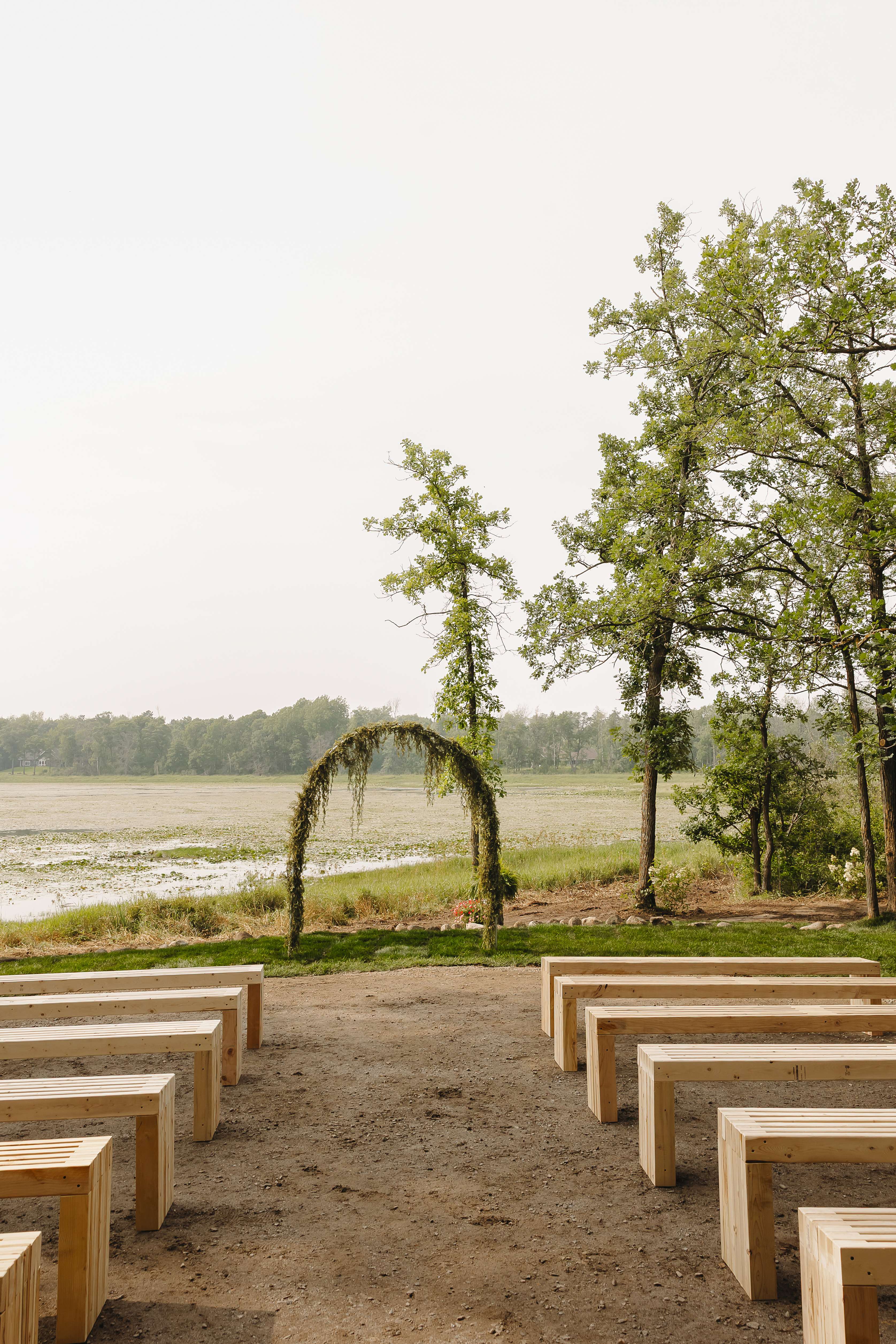 A greenery-draped ceremony arch overlooking the lake with natural-wood benches arranged for guests