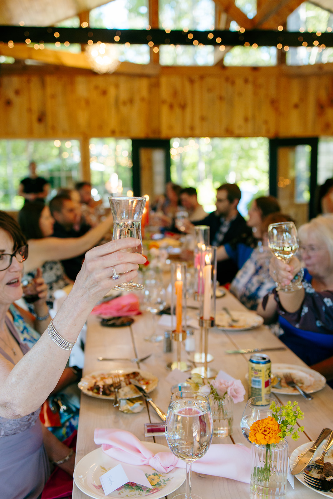 A guest raising a glass in a toast at a candlelit farm table inside the timber barn